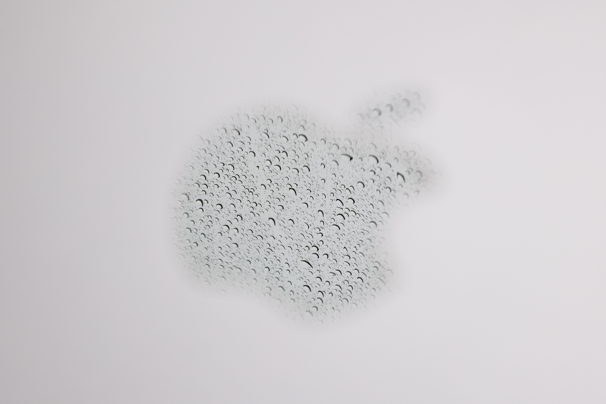 A reflection of rain in the Apple logo on a laptop photographed at f/13